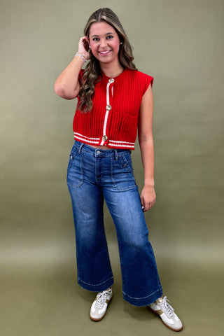 Woman wearing a red top with white buttons and blue jeans against a green background