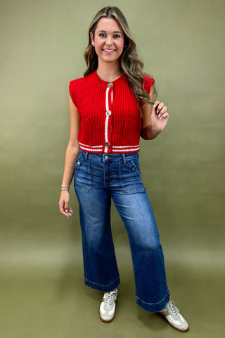 Woman wearing a red sleeveless top with white buttons and blue jeans on a green background