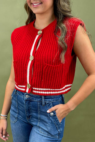 Person wearing a red knitted vest with white trim and blue jeans against a green background