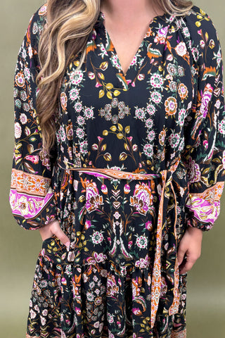 Woman wearing a dark floral dress with colorful patterns on a green background