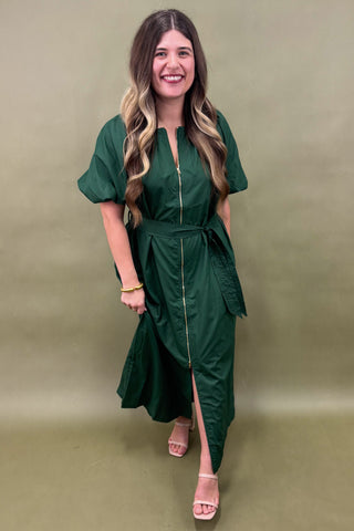 Woman wearing a green dress with a slit on a plain background