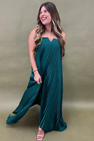 Woman wearing a teal pleated dress against a plain background