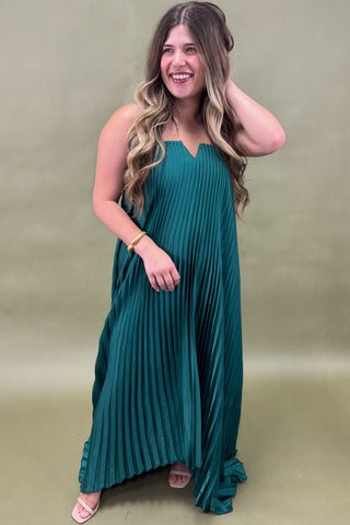 Woman wearing a teal pleated dress against a beige background