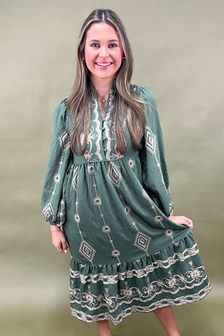 Woman wearing a green dress with white embroidery against a beige background