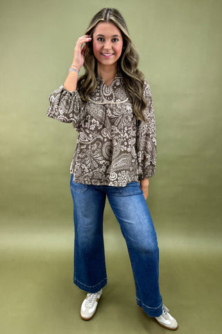 Woman wearing a patterned blouse and blue jeans against a green background