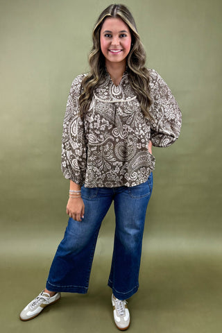 Woman wearing a patterned blouse and blue jeans against a green background