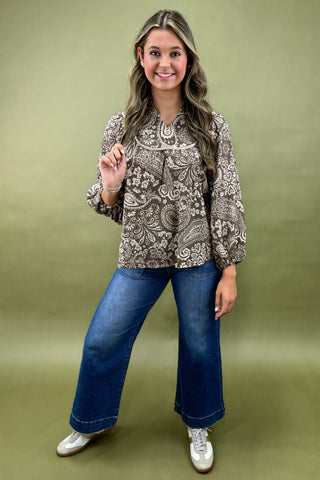 Woman wearing a patterned blouse and blue jeans against a green background