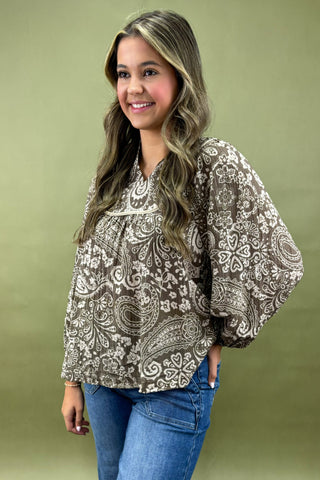 Woman wearing a patterned blouse and jeans against a green background