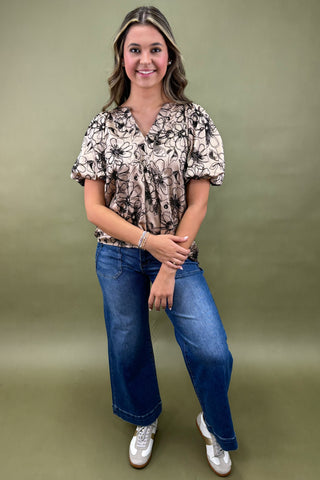Woman wearing a floral blouse and blue jeans against a green background