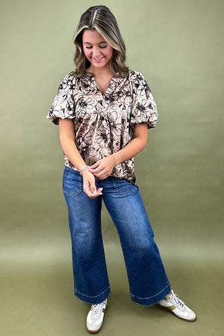 Woman wearing a patterned blouse and blue jeans against a green background