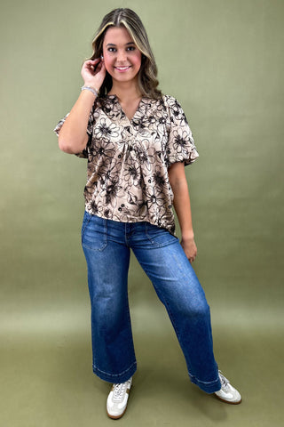 Woman wearing a floral blouse and blue jeans against a green background