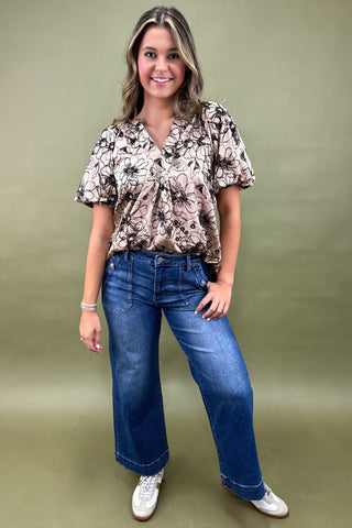 Woman wearing a floral blouse and blue jeans against a green background
