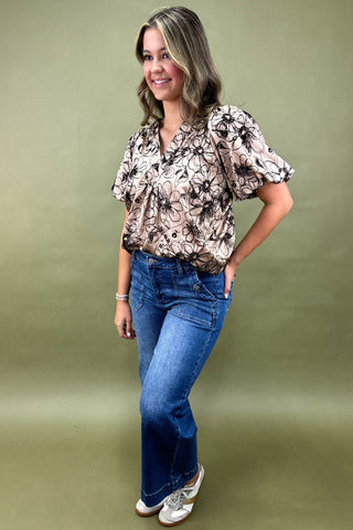 Woman wearing a floral blouse and blue jeans against a green background