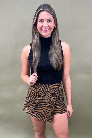Woman wearing a black top and zebra print shorts against a green background