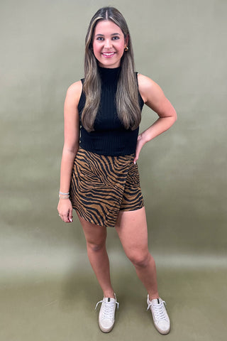 Woman wearing a black top and tiger stripe skirt against a plain background
