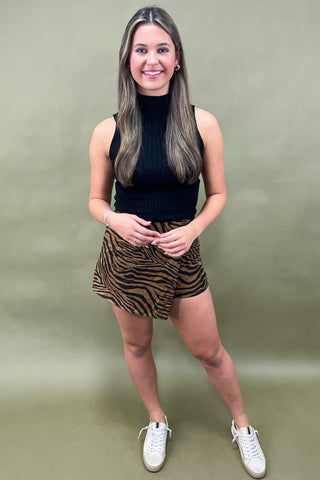 Woman wearing a black sleeveless top and zebra print shorts against a plain background