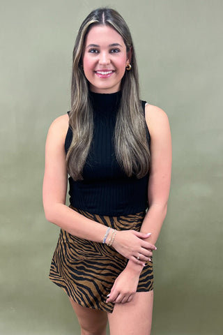 Woman wearing a black top and zebra print skirt against a green background