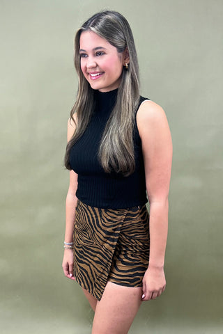 Woman wearing a black sleeveless top and zebra print shorts against a green background