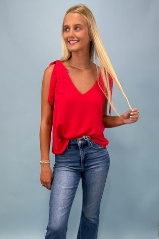 Woman wearing a red top and blue jeans against a gray background