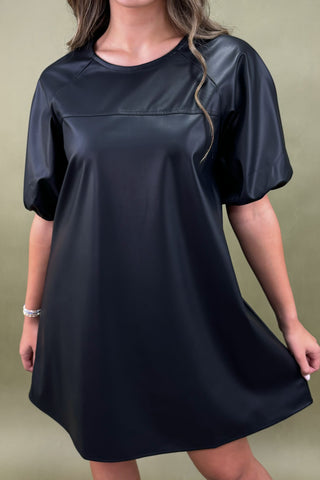 Black dress with leather-like panels worn by a person on a green background