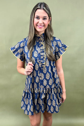 Woman wearing a blue dress with gold floral patterns against a green background