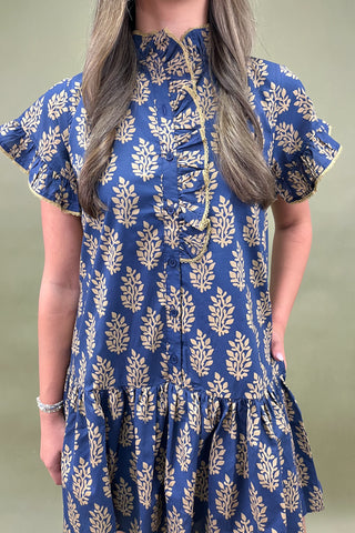 Woman wearing a blue dress with gold floral patterns against a plain background