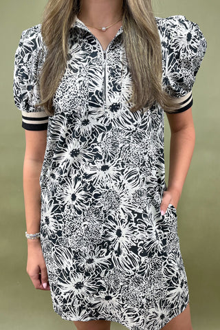 Woman wearing a black and white floral dress with short sleeves on a green background