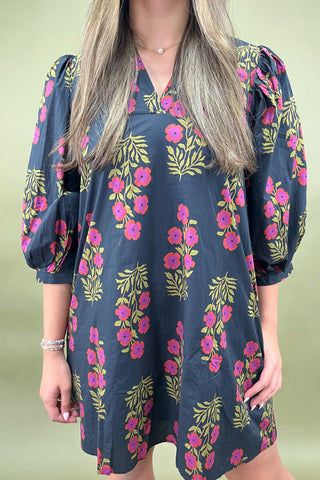 Woman wearing a navy dress with pink floral pattern against a light green background