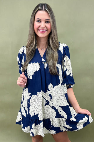 Woman wearing a navy blue dress with white floral pattern against a green background