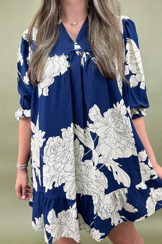 Navy blue dress with white floral pattern worn by a person on a beige background