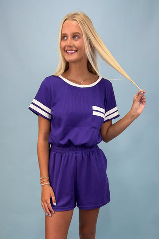 Woman wearing a purple outfit with white stripes on a plain background