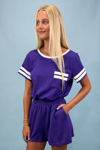 Woman wearing a purple outfit with white accents on a plain background