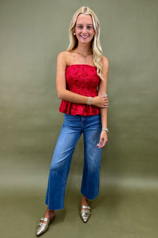 Woman wearing a red strapless top and blue jeans against a green background