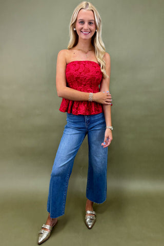 Woman wearing a red strapless top and blue jeans against a green background