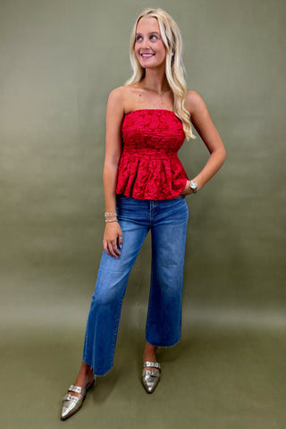 Woman wearing a red strapless top and blue jeans against a green background