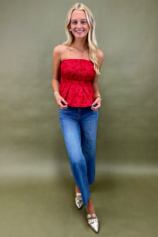 Woman wearing a red strapless top and blue jeans against a green background