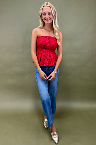 Woman wearing a red strapless top and blue jeans against a green background