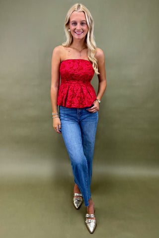 Woman wearing a red strapless top and blue jeans against a green background