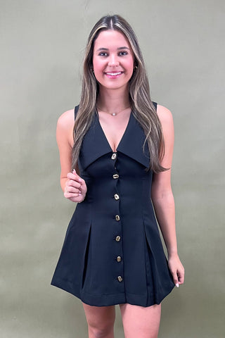 Woman wearing a black sleeveless dress with buttons against a green background