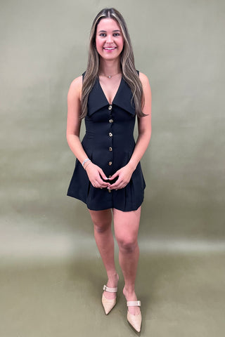 Woman wearing a black dress with gold buttons against a plain background