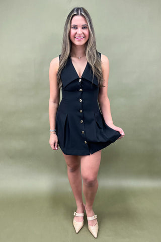 Woman wearing a black halter neck dress with buttons on a green background