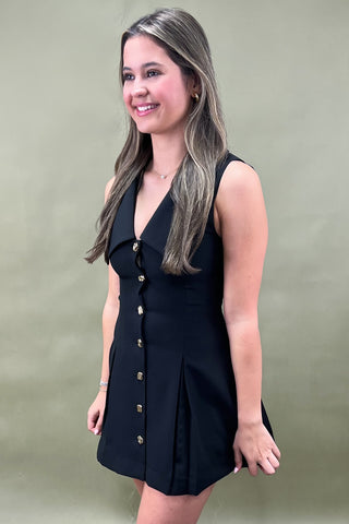 Woman wearing a black sleeveless dress with buttons against a green background