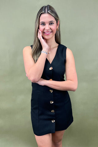 Woman wearing a black dress with gold buttons against a green background