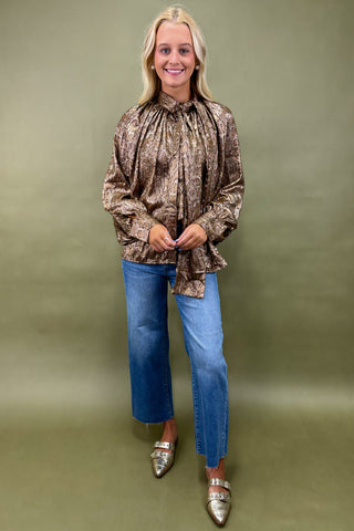 Woman wearing a patterned blouse and blue jeans against a green background