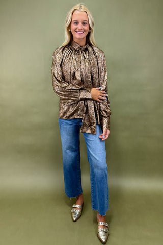 Woman wearing a patterned top and blue jeans against a green background