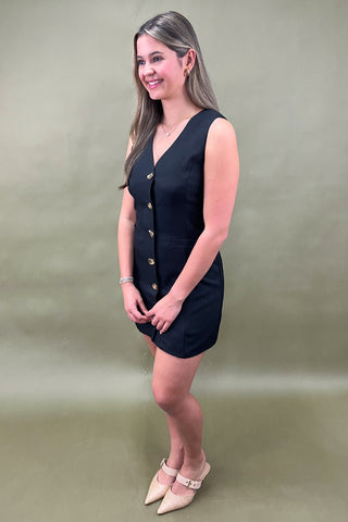 Woman wearing a black sleeveless dress with buttons on a beige background
