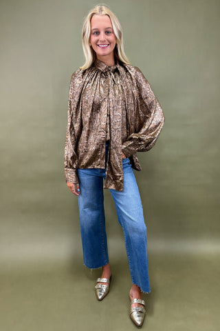 Woman wearing a patterned blouse and blue jeans against a green background