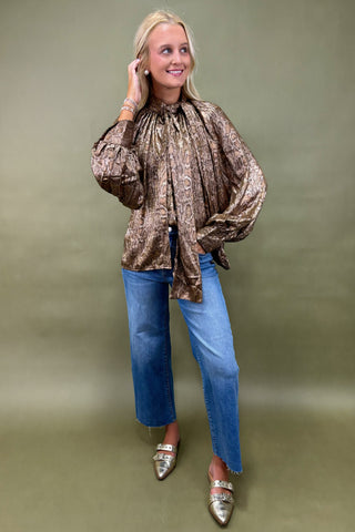 Woman wearing a patterned blouse, blue jeans, and metallic shoes against a plain background