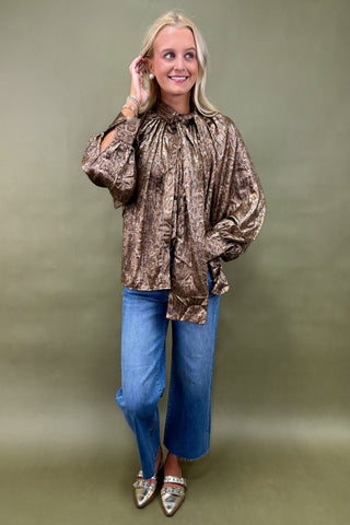 Woman wearing a patterned blouse and blue jeans against a plain background