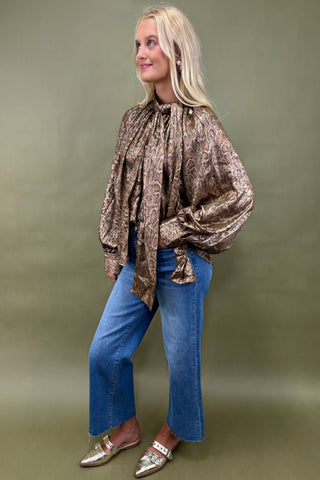 Woman wearing a patterned blouse and blue jeans against a green background